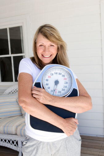 smiling woman in white clothes on porch hugging scale