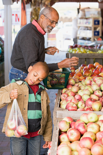 grandpa shopping at market for apples with grandson who is holding up a bag of apples
