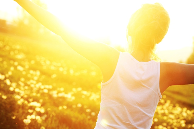 young woman with arms spread in field during sunset