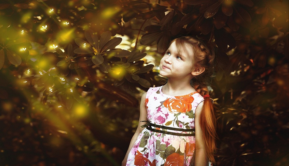 little girl standing in front a tree looking up towards sun