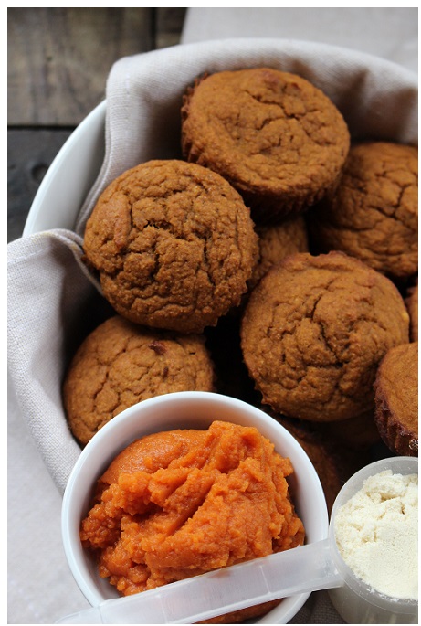 several cinnamon-colored, pumpkin protein muffins in bowel with white towel next to pumpkin puree and vanilla whey protein