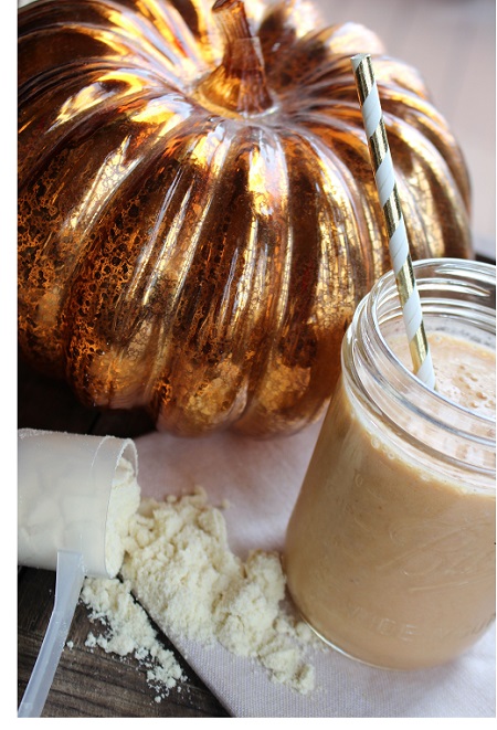creamy pumpkin whey protein shake in glass jar next to a scoop of vanilla whey protein and pumpkin ornament 