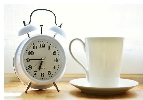 white alarm clock next to white coffee cup basking in sunlight