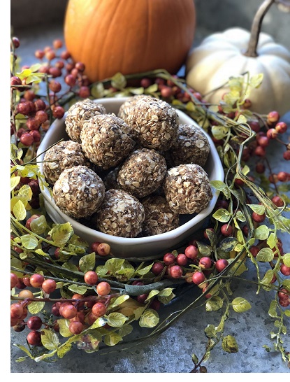 pumpkin spiced protein balls covered in oats and whey sitting in bowl surrounded by leaves, berries, and pumpkins