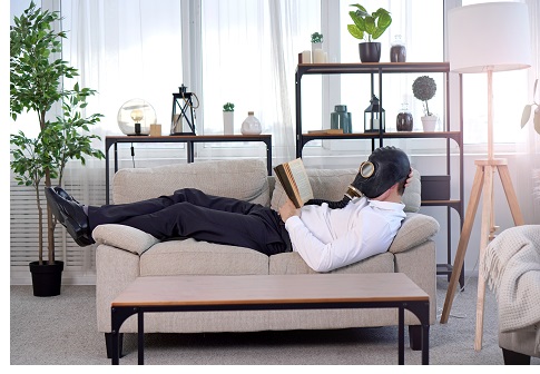 Pandemic coronavirus quarantine period concept. National quarantine concept. A man in a gas mask lies on a sofa and reads a book. Stay at home idea.