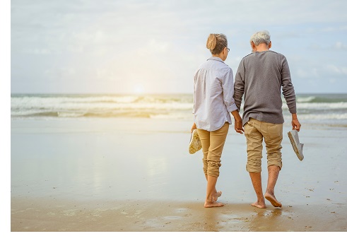 Senior couple walking on the beach holding hands at sunrise, plan life insurance at retirement concept.