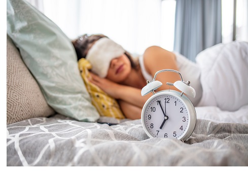 Sleeping peacefully. Alarm clock on bedside table with woman sleeping on background under warm blanket in comfortable bed, young female resting in bedroom, enjoying dreams