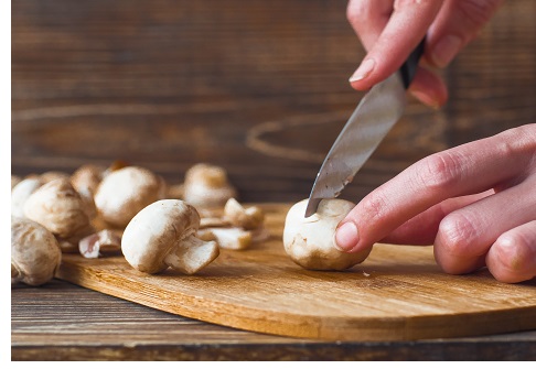 Woman hands slices mushrooms in kitchen. Female making mushroom sauce.